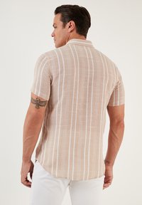 Camisa de manga corta, con cuello, en color beige claro con rayas verticales blancas, hecha de tela texturizada. Dobladillo redondeado en la parte posterior y ajuste entallado.