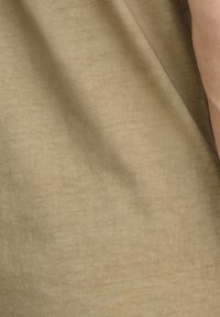 Tessuto beige con una superficie morbida e texture, caratterizzato da leggere pieghe e grinze. Braccio visibile all'estremità.