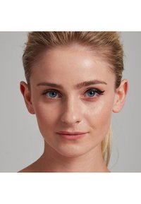 Porträt einer Person mit hellem Hautton, blauen Augen und nach hinten gestyltem blonden Haar, die kräftigen Eyeliner und einen glatten Teint aufweist.