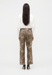 Παντελόνια με λεοπάρ σχέδιο, φαρδιά, σε μπεζ και μαύρο χρώμα, κατασκευασμένα από απαλή ύφανση. Συνδυασμένα με λευκό πουκάμισο και μαύρα παπούτσια με τακούνι.