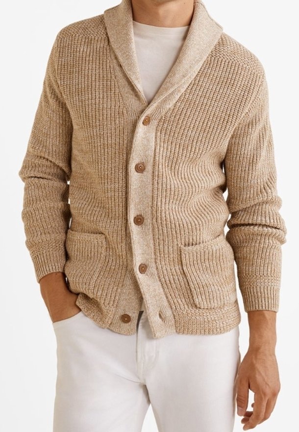 Cardigan beige en tricot avec col châle, devant boutonné et deux poches frontales. Tissu texturé et boutons en bois. Porté sur une chemise blanche.