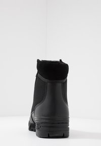 Svart ankelboot gjord av slät syntetiskt material med en mjuk ovandel och strukturerad sula. Har minimal sömnad och dragkedjestängning.