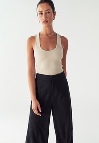 Bež majica brez rokavov z izrezom v obliki črke U, v kombinaciji z visokim pasom črnimi hlačami. Preprost dizajn, prilegajoča majica, široke hlace, ki lepo sodelujejo.