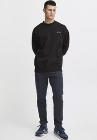 Sort sweatshirt med rund hals og broderet "A.R.C." logo. Sammen med marineblå joggers og sorte træningssko. Glat tekstur.