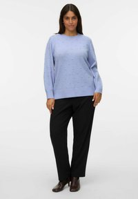 Maglione verde acqua a trama con puntini in rilievo, scollatura a girocollo e maniche lunghe, abbinato a pantaloni neri e calzature con tacco marroni.
