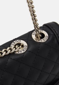 Sort quiltet læderhandtaske med sølvhardware, der har fremtrædende logo-detaljer og en flettet kædestrop.
