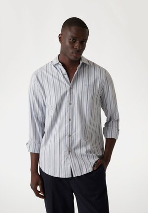 Camisa de botones rayada en azul claro, gris y blanco. Presenta un cuello clásico, mangas con puños y un logo sutil en el pecho.