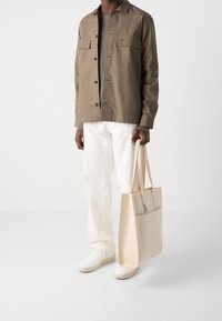 Hnědá bunda na knoflíky přes béžový pletený svetr, bílé kalhoty a bílé tenisky. Béžová taška typu tote se zipem a boční kapsou.