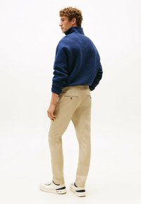 Pullover blu con motivo e colletto alto, pantaloni beige dritti e sneakers bianche. I pantaloni presentano tasche posteriori con chiusura a bottone.