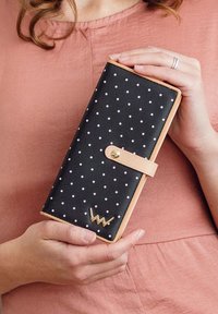Black wallet with white polka dots, beige accents, and a gold snap closure. Features a gold logo on the front.