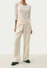 Helles beige gestreiftes Langarmhemd kombiniert mit lockeren kremfarbigen Hosen und schwarzen Plateauschuhen. Lässiger Stoff mit bequemem Schnitt.