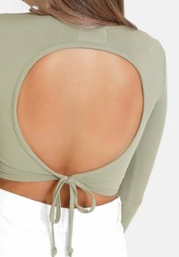 Långärmad topp i ljusgrön ribbad tyg med en stor u-ringning på baksidan, knuten i midjan med matchande band. Enkel och figurnära design.