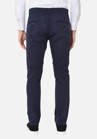 Pantaloni in cotone blu navy a vestibilità slim, con tasche posteriori con chiusura a bottone e una superficie liscia. Abbinati a scarpe bianche e nere.