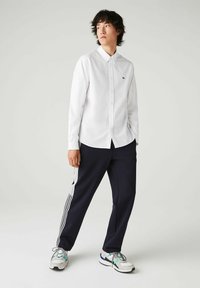 Witte overhemd met kraag, gecombineerd met donkerblauwe sportbroek met witte zijkanten, gedragen met grijze sneakers met gekleurde accenten.