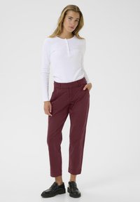 White long-sleeve henley top with buttons, paired with burgundy chinos and black loafers. Smooth texture and tapered fit.