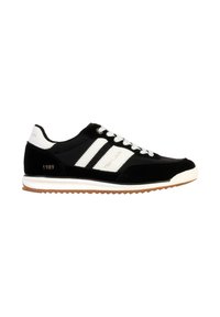Scarpe sportive nere con strisce bianche, parte superiore in suede e rete, suola in gomma bianca e suola di trazione marrone. Presentano un dettaglio "1989".