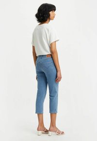 White short-sleeve shirt, light blue cropped jeans with a leather back patch, and white strappy sandals. Simple design, casual style.