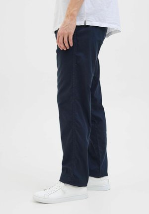 Temno modri bombažni hlače sproščenega kroja, z žepi na straneh in gladko teksturo, v kombinaciji z belimi supergami.