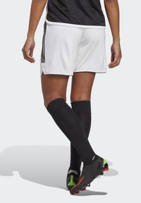 Schwarze und weiße Fußballshorts mit kontrastierenden Streifen, kombiniert mit schwarzen knielangen Socken und schwarzen Schuhen mit grünen Akzenten.