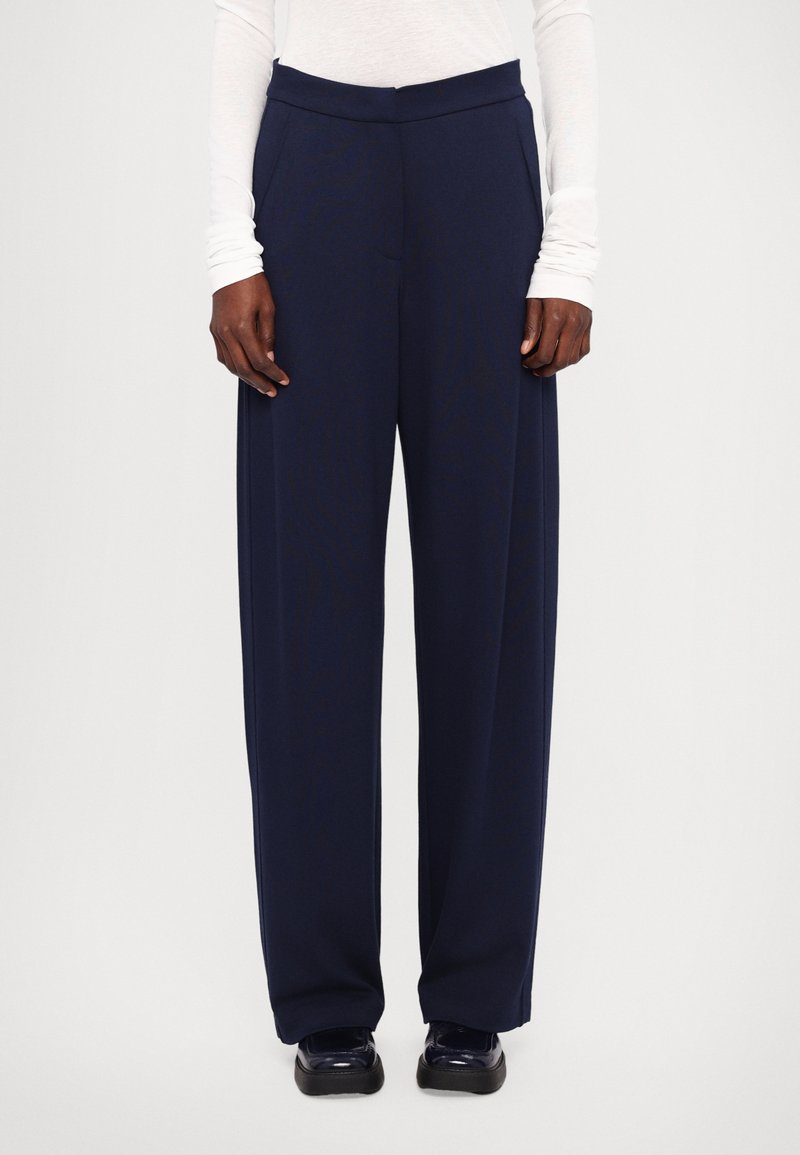 Wide-leg navy trousers with a smooth texture and elastic waistband, featuring front pockets and tailored seams for a structured look.