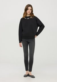 Czarna bluza z kwiatowymi zdobieniami przy dekolcie, w połączeniu z ciemnymi dżinsami i balerinami w kropki. Gładka tekstura, luźny krój.