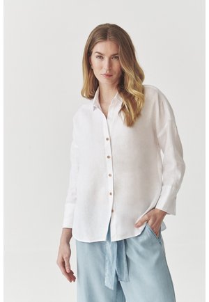 White linen button-up shirt with long sleeves, slightly oversized fit, featuring light brown buttons and a pocket on the left side.