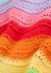 Tissu tricoté multicolore avec des rayures ondulées en lavande, rose, rouge, orange et jaune. Texture douce avec un motif ajouré réparti sur toute la surface.