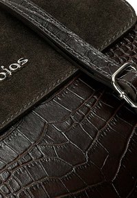 Brączowa torebka z teksturowanym wzorem krokodyla, zamszową klapą, srebrnymi metalowymi elementami i regulowanym paskiem. Posiada tłoczone logo.