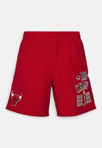 Röda shorts i lättviktig tyg, med en tjur-logotyp på vänstra benet och text som hyllar mästerskapsår på högra sidan.