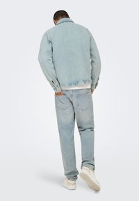 Jasnoniebieska kurtka dżinsowa z kołnierzem i ściągaczami przy rękawach, zestawiona z dopasowanymi, luźnymi jasnoniebieskimi dżinsami oraz białymi trampkami.