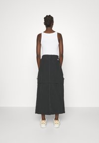 Gonna lunga nera con tasche cargo, vita elasticizzata, a due strati, abbinata a una canotta bianca e sneakers chiare.