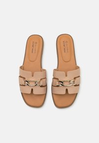 Sandales en mousse véganes de couleur beige clair avec deux larges sangles et un accent de chaîne dorée. Semelle intérieure texturée et semelle plate marron.