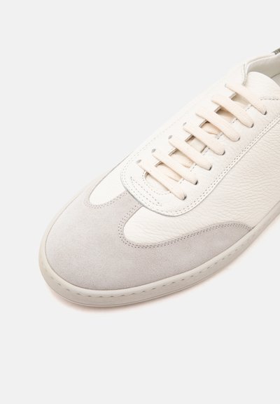 Baskets en cuir blanc et daim gris clair avec lacets et coutures blanches assortis sur un fond uni clair.