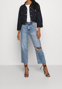 Tmavě modrá džínsová krátká bunda se dvěma předními kapsami, ve spojení s světle modrými džíny širokého střihu s potrhanými detaily. Celý vzhled doplňují černé sandály na podpatku s pásky.