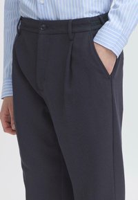 Marineblauwe geplooide broeken van een gestructureerde stof, met een knoopsluiting, zijzakken en een elastische tailleband voor comfort.