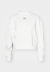 Sudadera corta de manga larga blanca con puños y cuello acanalados, que presenta un pequeño emblema metálico cuadrado en el pecho.
