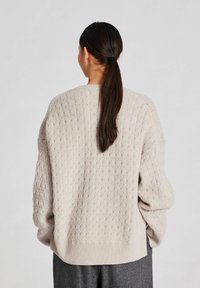 Lysegrå strikket sweater med et struktureret mønster, brede ærmer og en afslappet pasform. Ribbet kant og manchetter tilføjer detaljer.