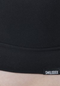 Zwarte aansluitende tailleband met een gladde textuur, voorzien van een klein wit label met "SMILODOX" aan de zijkant, benadrukkend minimalistisch design.