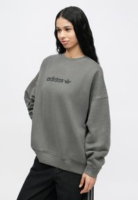 Γκρι φούτερ από μαλακό ύφασμα, με στρογγυλή λαιμόκοψη και άνετη, φαρδιά γραμμή. Μαύρο λογότυπο "adidas" τυπωμένο μπροστά.
