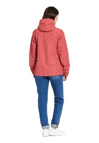 Rode waterdichte jas met capuchon, elastische manchetten en een logo op de rug, gecombineerd met blauwe jeans en witte sneakers. Getextureerde stof.