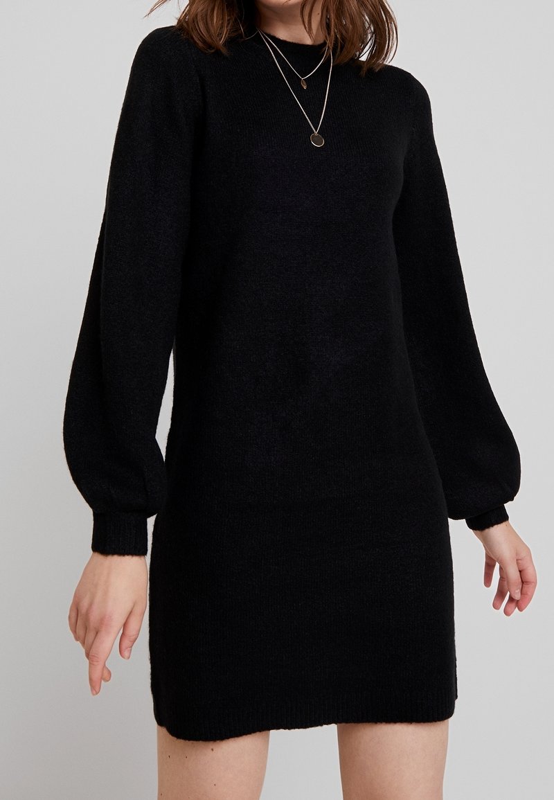 Robe pull noire en maille avec un col rond, de longues manches ballon et une silhouette ajustée, dotée de poignet et d'ourlet côtelés. Texture douce.