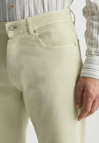 Jeans beige claro con corte recto, hechos de denim, con un bolsillo frontal, pasadores para cinturón y un cierre de botón metálico.