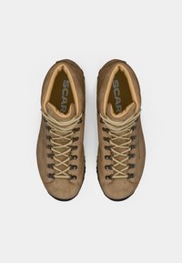 Ein Paar braune Wildleder-Wanderstiefel mit beigen Schnürsenkeln, Metallhaken und gepolsterten Knöchelkragen, von oben auf einem weißen Hintergrund gesehen.
