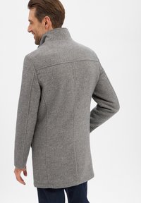 Grijze wolblend jas met een hoge kraag, gestructureerde schouders en een rechte snit. Heeft een subtiele visgraatstructuur en zijzakken.