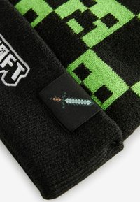 Fleece-Decke mit schwarzem Grund und grünen, pixelierten Mustern sowie einem weißen, gestickten Logo. Enthält ein schwarzes Etikett mit einem Schwert-Design.