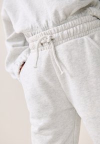Jogging light gris en tissu doux, avec une taille élastique dotée d'un cordon de serrage et des poches latérales. Texture et motif subtils visibles.
