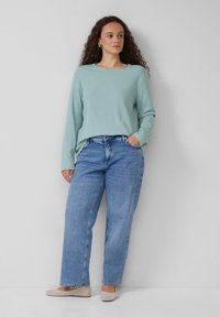 Hellblaues, geripptes Langarmshirt kombiniert mit lockeren blauen Jeans und beigen flachen Schuhen. Einfaches, lässiges Outfit mit lockerem Schnitt.