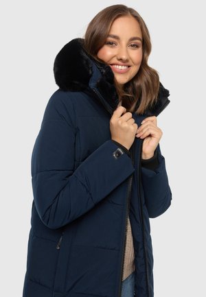 Navy puffer jacket with a detachable black faux fur hood, zippered front, and quilted design. Ribbed cuff accents and side pockets.