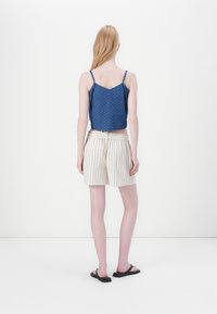 Camisole bleu à pois avec des fines bretelles associé à un short rayé beige. Le modèle se tient de dos, portant des sandales noires.