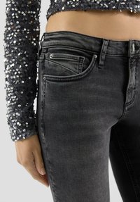 Czarne jeansy z denimu o dopasowanym kroju, z przednią kieszenią i subtelnymi detalami przeszyć. Połączone z długim topem z cekinami.